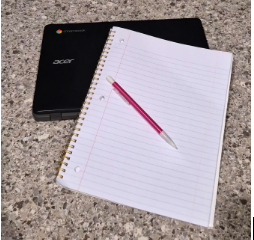 A closed laptop sits under a notebook and pencil, representing the traditional paper and pencil method of school, which is proven to support deeper learning.