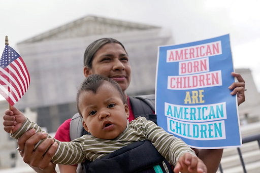(A mother and her son, who was granted citizenship due to the birthright citizenship clause, protesting outside the Supreme Court Building)